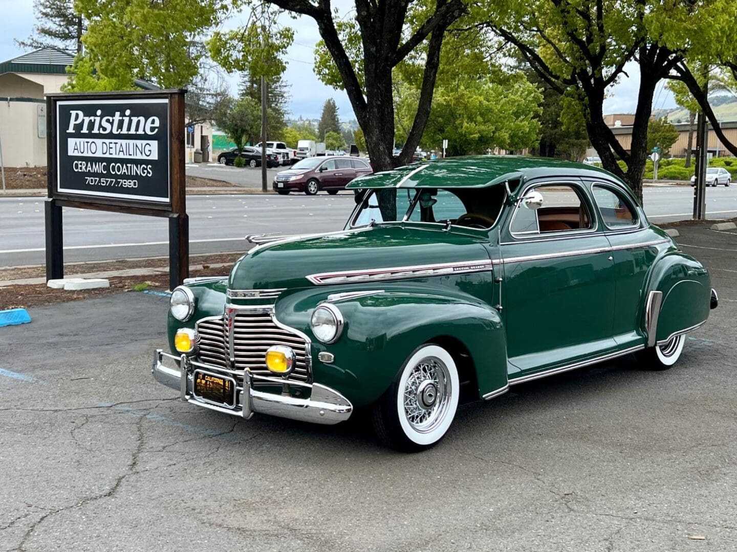 Green classic car parked by auto detailing sign